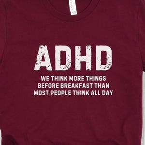 May include: Burgundy t-shirt with white text that reads "ADHD We think more things before breakfast than most people think all day."