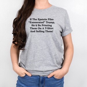 May include: A gray t-shirt with the text "If The Epstein Files 'Exonerated' Trump, He'd Be Printing Them On A T-Shirt And Selling Them!" in black. The shirt is worn by a person.