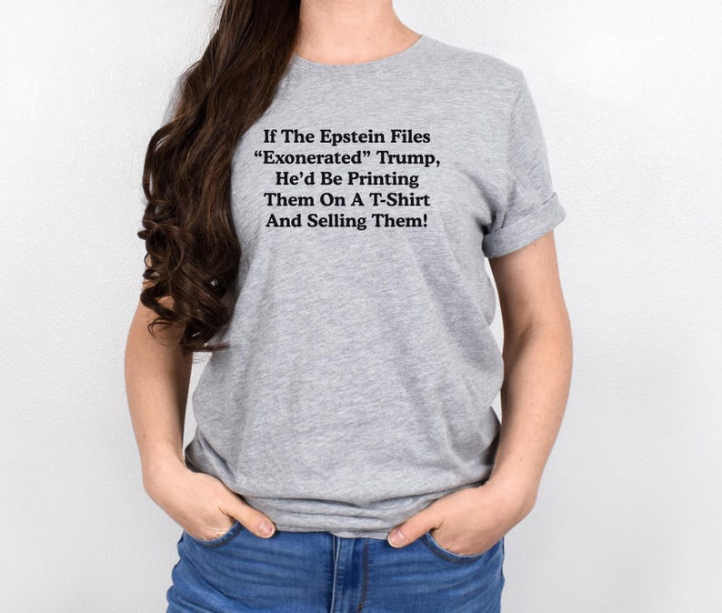 May include: A gray t-shirt with the text "If The Epstein Files 'Exonerated' Trump, He'd Be Printing Them On A T-Shirt And Selling Them!" in black. The shirt is worn by a person.