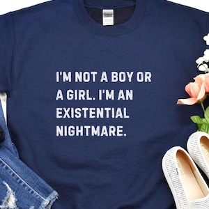 May include: Navy blue sweatshirt with the text "I'M NOT A BOY OR A GIRL. I'M AN EXISTENTIAL NIGHTMARE." in white block letters. The sweatshirt is a crew neck style.