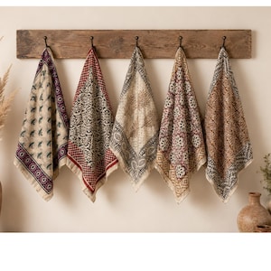 May include: Five patterned cloths hanging from a wooden rack. The cloths feature various designs in cream, red, and brown. The cloths are made of a soft material, likely used as kitchen towels or decorative accents. The cloths are hanging on a wooden rack.