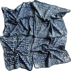 May include: Four indigo blue and white patterned scarves are arranged in a square. Each scarf features a unique design, including floral, geometric, and wave patterns. The scarves are made of a soft, flowing fabric.