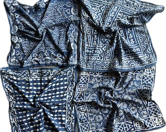 May include: Four indigo blue and white patterned scarves are arranged in a square. Each scarf features a unique design, including floral, geometric, and wave patterns. The scarves are made of a soft, flowing fabric.