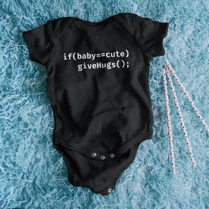 Peut inclure: Combinaison noire pour bébé avec un texte blanc qui dit "if(baby==cute) giveHugs();". La combinaison est sur une surface bleue et duveteuse.