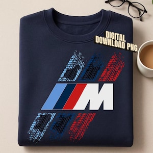 May include: A navy blue sweatshirt featuring a graphic design of the letter M in white, preceded by three diagonal stripes in light blue, dark blue, and red. The design includes textured tyre track patterns in matching colours. Text reads DIGITAL DOWNLOAD PNG.