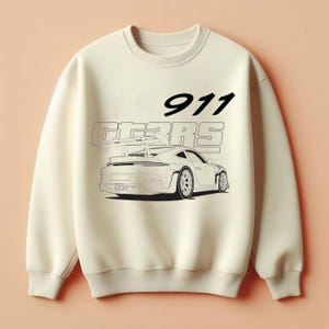 Könnte beinhalten: Cremefarbenes Sweatshirt mit einer schwarz-weißen Grafik eines Sportwagens und dem Text "911 GT3RS". Das Design ist mittig auf der Vorderseite des Rundhals-Sweatshirts angeordnet.