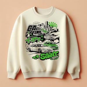 May include: Cream-colored sweatshirt featuring a graphic design with two cars, city skyline, and Japanese text. The design includes green and black accents, with the word "Saint" in green. The sweatshirt has a crew neck and long sleeves.