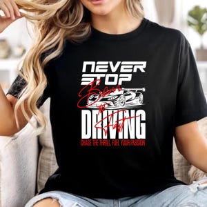 May include: Black t-shirt with the text "NEVER STOP BELIEVING # DRIVING" in white and red. A white race car graphic is featured above the word "DRIVING". The phrase "CHASE THE THRILL FUEL YOUR PASSION" is printed at the bottom.