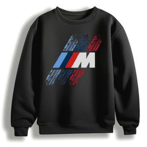 Könnte beinhalten: Ein schwarzes Langarm-Sweatshirt mit einer großen Grafik auf der Brust. Die Grafik zeigt den Buchstaben M in Weiß, davor drei diagonale Streifen in Hellblau, Dunkelblau und Rot, die alle mit einem strukturierten Reifenprofil überlagert sind.