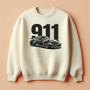 Op de afbeelding: Crèmekleurige sweatshirt met een zwarte sportwagenafbeelding met rode remklauwen en het nummer "911" in grote zwarte letters. De auto heeft een strak, modern ontwerp tegen een neutrale achtergrond.