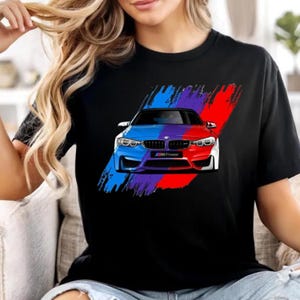 May include: Black t-shirt featuring a split-color graphic of a BMW M series car. The car is divided into blue and red sections, with a purple stripe in between. The design includes the text "M Power".
