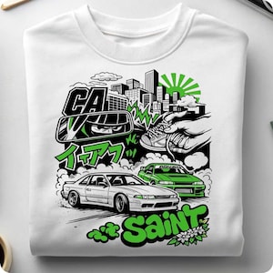 May include: White sweatshirt with a graphic design featuring two cars, a cityscape, and Japanese text. The design incorporates green and black elements, with the word "SAINT" in a stylized font.