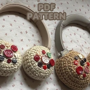 Puede incluir: Dos pares de auriculares con cubiertas de oreja de ganchillo adornadas con botones coloridos. Los auriculares tienen una combinación de colores neutros, con cubiertas de oreja crema y beige. El texto "PDF PATTERN" es visible.