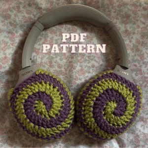 May include: Gray Sony headphones with crocheted ear covers. The ear covers feature a spiral design in shades of purple and green. The text "PDF PATTERN" is displayed across the top of the image.
