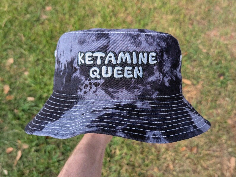 May include: A black and white tie-dye bucket hat with the text "Ketamine Queen" embroidered in white.