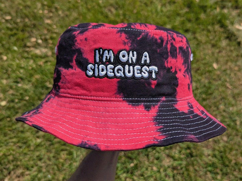 May include: Red and black tie-dye bucket hat with the text "I'm on a Sidequest" embroidered in white.