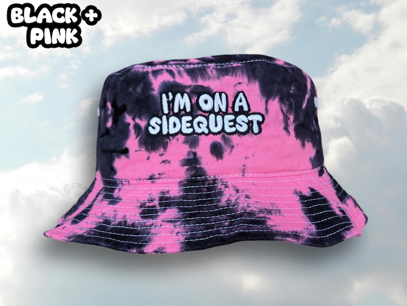 May include: Black and pink tie-dye bucket hat with the text "I'm on a Sidequest" embroidered in white.