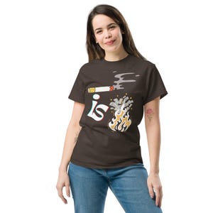 Puede incluir: Una camiseta marrón con un gráfico de un cigarrillo fumando un montón de dinero en llamas. El texto "is" está escrito en una fuente estilizada sobre el gráfico.