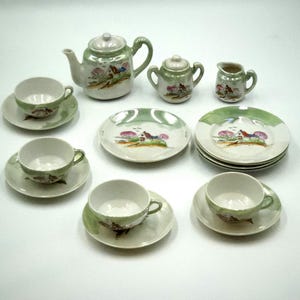 Peut inclure: Un service à thé miniature en porcelaine comprenant une théière, un sucrier, un pot à lait, quatre tasses, quatre soucoupes et trois assiettes. Chaque pièce est ornée d'un paysage peint à la main avec maison, arbres et accents verts.