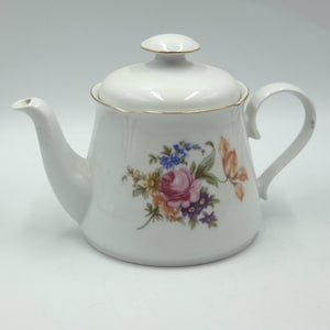 Puede incluir: Tetera de cerámica blanca con tapa, con un diseño floral en rosa, azul y naranja. La tetera tiene un asa y un pico curvos, con ribete dorado. Un accesorio de té clásico.