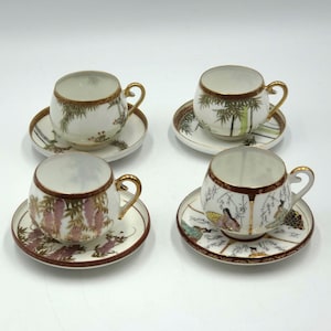 Peut inclure: Quatre tasses à thé et soucoupes en porcelaine vintage. Chaque tasse et soucoupe présente un motif peint à la main unique avec une bordure dorée. Les motifs comprennent du bambou, des glycines et des oiseaux. Les tasses ont des anses dorées.