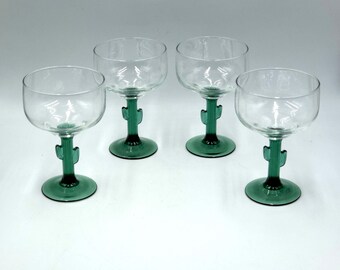 May include: Four clear margarita glasses with green cactus-shaped stems and bases. The glasses have a rounded bowl shape. The cactus stems are a vibrant green color, adding a unique touch to the glassware.