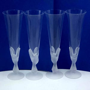 May include: Four clear champagne flutes with a frosted floral design at the base. The flutes have a tall, slender shape and are made of transparent glass. The design adds a touch of elegance to the glassware.
