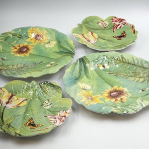 May include: Set of four green ceramic plates with floral and butterfly designs. The plates have a scalloped edge and are perfect for serving appetizers, desserts, or snacks.