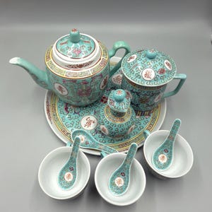 May include: A turquoise tea set comprising a teapot, cup, creamer, sugar bowl, serving tray, spoons, and bowls. The set has floral and geometric patterns with gold trim. The bowls and spoons are white with turquoise accents.