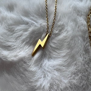 May include: A gold chain necklace with a lightning bolt pendant.