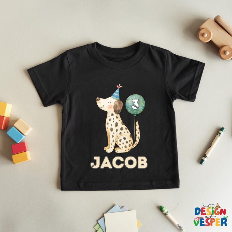 May include: Black toddler t-shirt featuring a Dalmatian dog wearing a party hat and holding a balloon with the number 3. The name "JACOB" is printed below the dog in white letters. The shirt is a birthday theme.