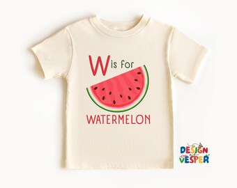 以下が含まれることがあります： クリーム色の幼児用Tシャツ。スイカのデザインで、赤い文字「W」、赤い文字で「is for」と「watermelon」、黒い種と緑色の皮を持つスイカのスライスが描かれています。子供向けのTシャツです。