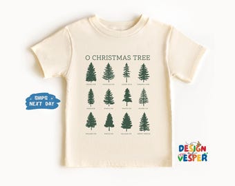 以下が含まれることがあります： 「O CHRISTMAS TREE」の文字と、さまざまな種類のクリスマスツリーのイラストが描かれたクリーム色のTシャツ。グランドファー、ダグラスファー、フレイザーファーなどの木の名前が記載されています。