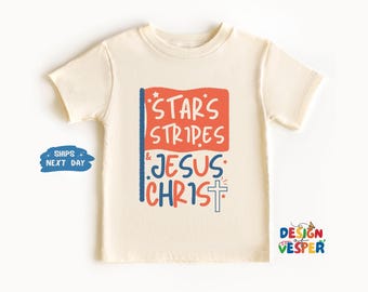 Puede incluir: Camiseta color crema con el texto "Stars Stripes & Jesus Christ" en rojo, azul y blanco. El diseño incluye un gráfico de bandera y una cruz. La camiseta es de manga corta y tiene cuello redondo.