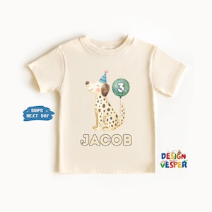 May include: Cream-colored toddler t-shirt featuring a watercolor illustration of a Dalmatian dog wearing a party hat and holding a number 3 balloon. The name "JACOB" is printed below the dog in a bold font. The shirt is a short-sleeved design.