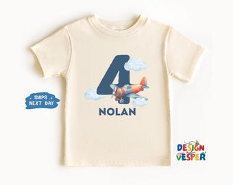 May include: Cream-colored toddler t-shirt featuring a blue number 4 with a watercolor airplane design. The airplane is red and gray, with white clouds. The name "NOLAN" is printed below the airplane. The shirt has short sleeves.