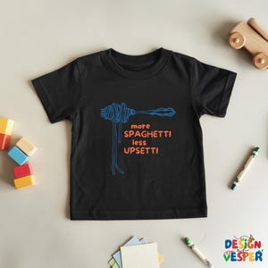 Pu&ograve; includere: T-shirt nero per bambini con grafica blu di spaghetti e forchetta e la scritta arancione "more spaghetti less upsetti". La maglietta &egrave; realizzata in materiale morbido.
