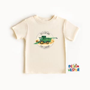 May include: Cream-colored t-shirt featuring a green combine harvester illustration within a circular design. The text reads "JUST A BOY WHO LOVES COMBINES". The shirt has short sleeves and a crew neck, suitable for children.