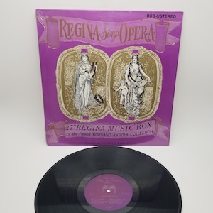 Może przedstawiać: Fioletowa okładka płyty winylowej z pozłacanymi napisami: "REGINA Sing OPERA" i "27" REGINA MUSIC BOX Of the Famed BORNAND ANTIQUE COLLECTION NOSTALGIC ARIAS FROM THE VELVET & GOLDEN AGE". Okładka zawiera dwie ilustracje kobiet w ozdobnych złotych ramach.