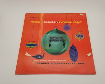 May include: A red vinyl record album cover with a green, round, Christmas ornament featuring a black and white music box. The album cover has the text "The Original Music Box Medley of Christmas Songs" and "Faithfully reproduced from Rare Old Music Boxes in the FAMOUS BORNAND COLLECTION".