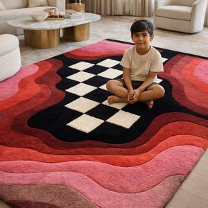 May include: A vibrant, multi-colored area rug with a unique wave design. The rug features a gradient of pink, red, and black hues, with a central checkered pattern. The rug is a statement piece for any living space.