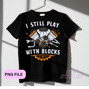 Peut inclure: T-shirt noir avec un graphique blanc d'un moteur et le texte "I still play with blocks".