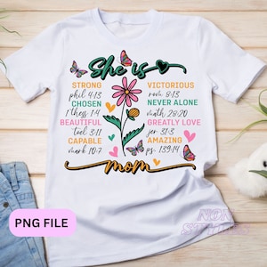 Op de afbeelding: Wit T-shirt met een bloemenontwerp en de tekst "She is", gevolgd door een lijst met woorden en bijbelverzen die een sterke vrouw beschrijven. De tekst "mom" staat onderaan het ontwerp.