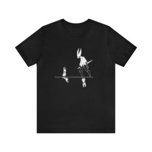 Op de afbeelding: Zwart T-shirt met een witte afbeelding van twee figuren, een groter dan de andere, die op een reflecterend oppervlak staan. De figuren zijn gestileerd en lijken op personages uit een videogame.