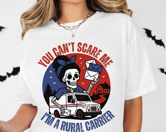 May include: White t-shirt with a graphic featuring a skeleton rural carrier in a postal truck, holding mail. The design includes the text "YOU CAN'T SCARE ME I'M A RURAL CARRIER" in red and blue, with a Halloween theme.