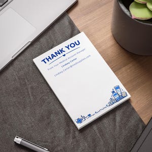 May include: A white notepad with blue text that reads "THANK YOU" and contact information. The notepad has a medical theme with blue illustrations of medical supplies and a heartbeat line.