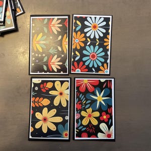 May include: Four rectangular cards with floral designs. Each card has a black border and a black background. The floral patterns feature various colors, including yellow, orange, red, blue, and white.