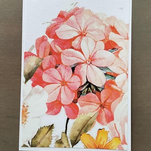 May include: A greeting card featuring a watercolor floral design. The card showcases a cluster of pink and orange flowers with green and yellow accents. The flowers are set against a white background.
