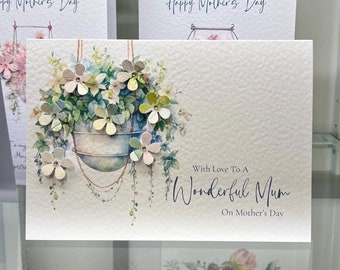 May include: A white card with a watercolor illustration of a hanging planter with flowers. The text "With Love To A Wonderful Mum On Mother's Day" is printed on the card.