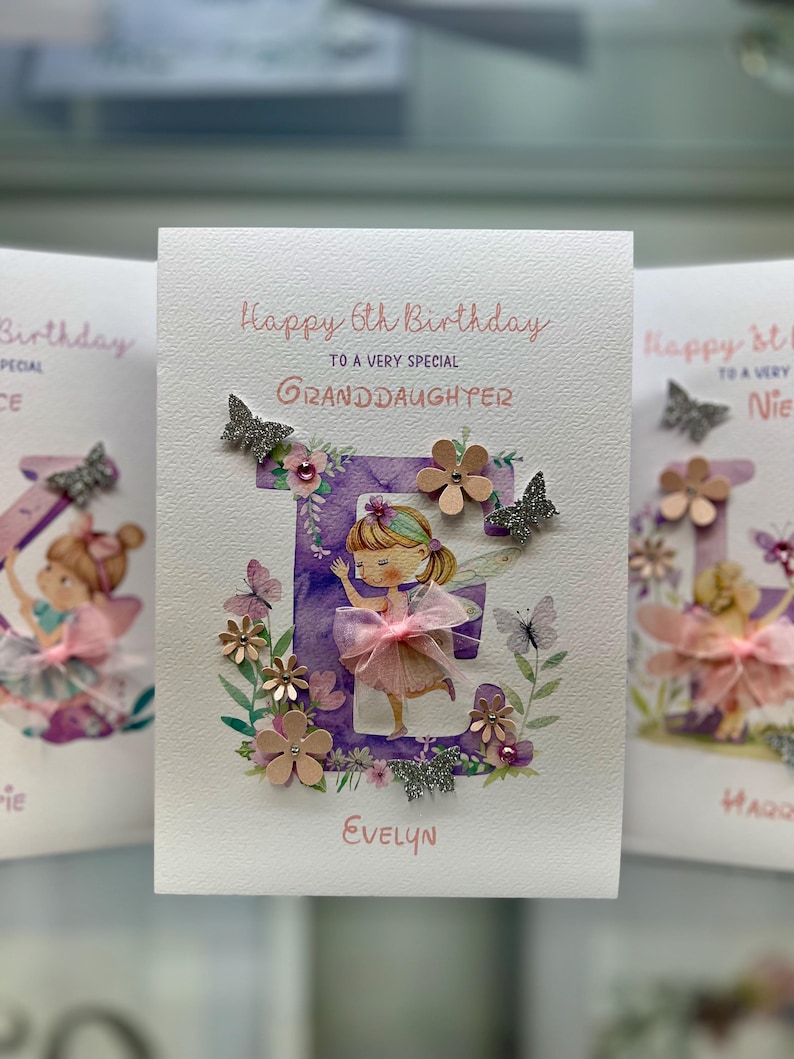May include: A handmade birthday card with a purple letter E decorated with flowers, butterflies, and glitter. The letter E is surrounded by a watercolor floral design. The card says "Happy 6th Birthday to a very special Granddaughter" and is signed "Evelyn".